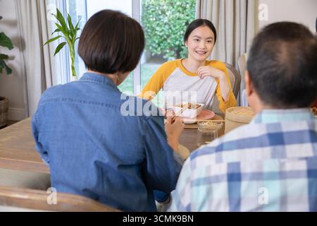Asian family sitting around dining table at home sharing meal with bento box and chopsticks Stock Photo