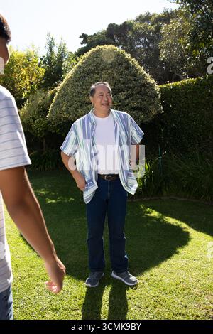 Asian father standing and son walking in backyard garden under sunlight Stock Photo