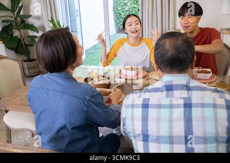 Asian family of four sharing noodle bowls and using chopsticks around dining table at home Stock Photo