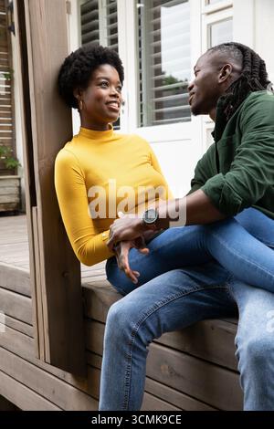 African american couple holding hands and gazing at each other on porch bench, sporting wristwatch Stock Photo
