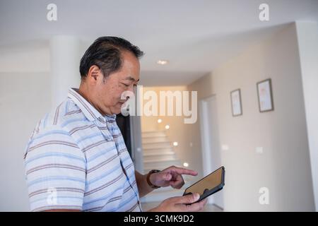 Middle-aged asian man standing in modern hallway using digital tablet near support column Stock Photo