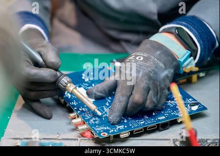 Skilled technician repairs electronic circuit board with soldering tool in workshop Stock Photo