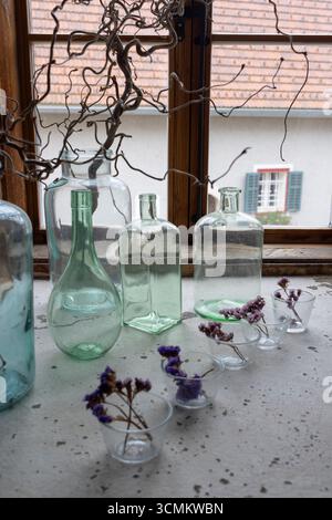 Various empty glass bottles and small purple flowers decorating a windowsill in Heimschuh, Styria, Austria Stock Photo