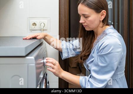 Female pressing button on washing machine to start laundry, concept of household chores and home cleaning Stock Photo