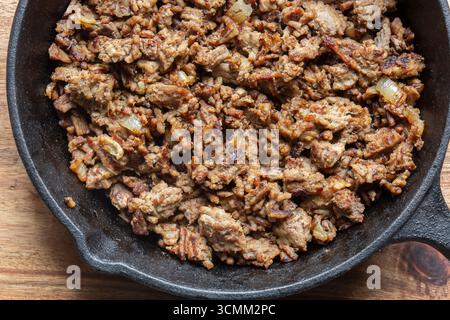 Beef mince with onion fried in a cast iron frying pan. On a wooden board background backdrop. Stock Photo