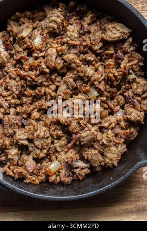 Beef mince with onion fried in a cast iron frying pan. On a wooden board background backdrop. Stock Photo