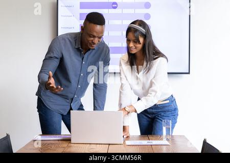 Diverse coworkers leaning over table in boardroom analyzing data on laptop, screen with charts Stock Photo