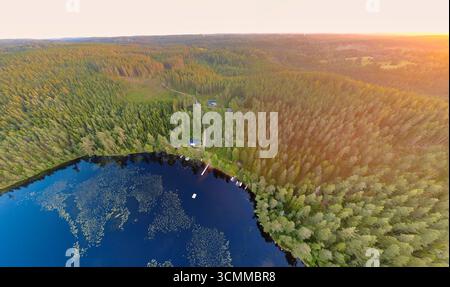Aerial view of a tranquil forest lake in the evening light. Golden rays of sunshine, cottages on the shore, and autumn-colored trees create a peaceful Stock Photo