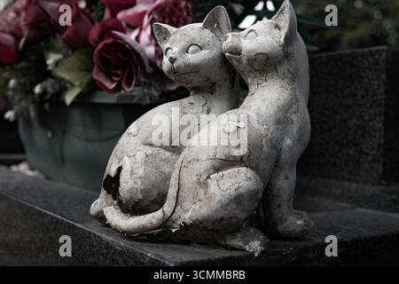 Memorial Sculpture of two stone cats resting eternally together with fresh Roses on a grave marker Stock Photo