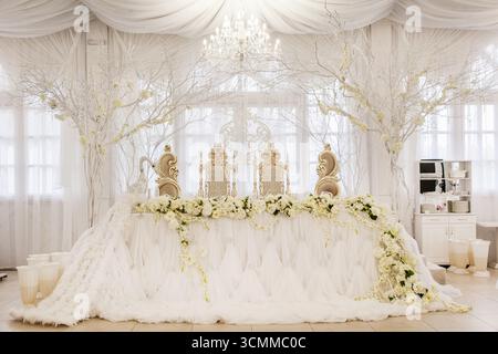 Stunning wedding setup featuring an intricately designed backdrop adorned with white flowers and elegant decorations. Stock Photo