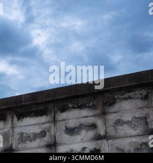 Old grey concrete blocks wall with cloudy blue sky Stock Photo