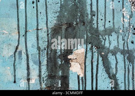 Dirty black spray paint with drips on a blue wall texture Stock Photo