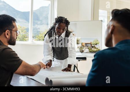 Three individuals discussing architectural plans and designs in a bright and modern workspace, highlighting teamwork and creativity. Stock Photo