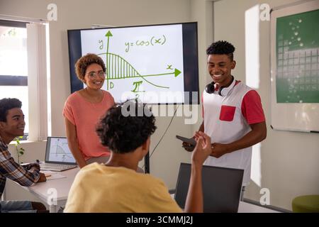 Diverse teacher and students analyzing cosine graph on monitor at table in classroom with laptop Stock Photo