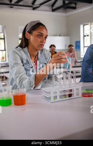 Diverse teenage classmates using pipette and transferring liquids into test tube rack on lab bench Stock Photo