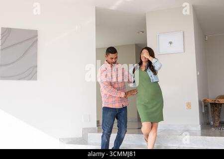 Diverse couple stepping down marble steps in foyer with tile floor, smiling together Stock Photo