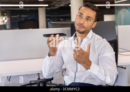 Man in shirt with smartphone horizontally and gesturing at office desk with monitors, copy space Stock Photo