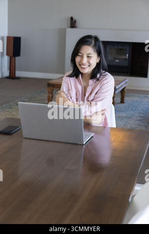 Woman Using Computer Work Person working on a laptop at a dining table in a home setting, using a ...