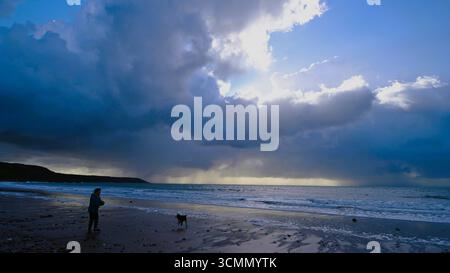 Woman and dog on Port-Eynon beach on the Gower with low and heavy cumulonimbus clouds over Port-Eynon Bay. Stock Photo