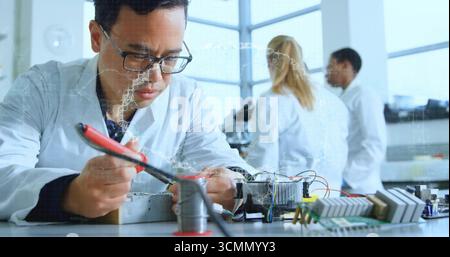 Soldering technician in lab coat using soldering iron leaning over lab bench with circuit boards Stock Photo