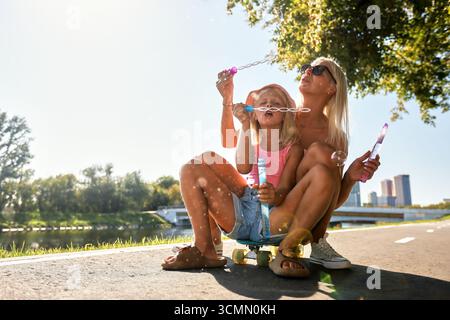 Mother and daughter having fun blowing bubbles outdoors in the summer sun Stock Photo
