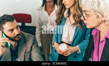 A diverse group of business professionals huddle together to listen in on an important conference call while solving a problem in a modern office meet Stock Photo