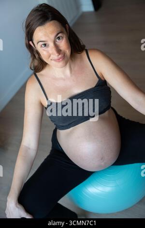 Vertical picture of a pregnant woman doing healthy exercises with pilates ball at home Stock Photo