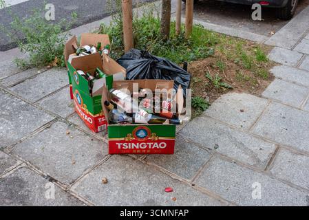 Empty Asahi and Tsingtao beer bottles left behind in boxes on the pavement in Paris. Littering Stock Photo