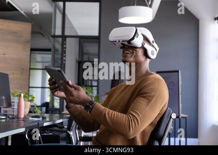 African american man using vr headset and tablet at office desk interacting vr environment Stock Photo