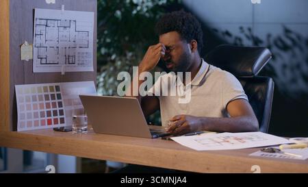 African American architect business man laptop work overtime in night office tired businessman overwork exhausted male guy discomfort evening take off Stock Photo