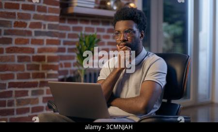 African American businessman night office manager business man thinking pensive thoughtful searching idea insight online trading laptop work studying Stock Photo