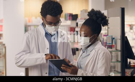 Doctors in masks covid health care pharmacy consultants physicians using digital tablet medicine pills drugs inventory male female pharmacists African Stock Photo