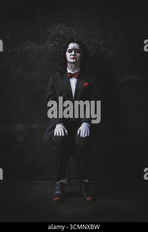YORK, UK - AUGUST 31, 2025. A male cosplayer dressed as Billy The Puppet from the Saw horror movie films sitting in a scary dark room with copy space Stock Photo