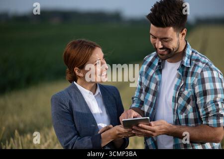 Friendly farmer and businesswoman talking about land prices while standing in a field. The woman looking at man while he enthusiastically points to ta Stock Photo