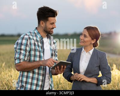 Handsome farmer and young businesswoman smiling politely at each other when discussing crop prices while standing in wheat field. Agricultural busines Stock Photo