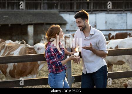Farmers discussing business next to cattle pen fence. Woman is holding a tablet while listening to man speaking enthusiastically Stock Photo