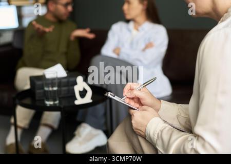 Female Psychologist Taking Notes during Multiethnic Couple Counseling Stock Photo