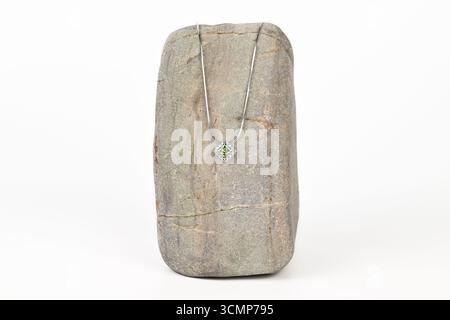 A necklace is displayed on a rock. The necklace is silver and has a green stone. The rock is grey and has a rough texture. The necklace and rock toget Stock Photo