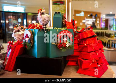 Colorful holiday gift boxes on festive display in a modern shopping mall, decorated with ribbons, wreaths, and seasonal ornaments. Stock Photo