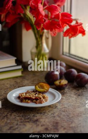 Homemade plum pie with gladiolus flowers and fresh plums on kitchen table. Stock Photo
