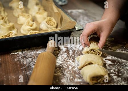 Placing cinnamon roll slices on baking tray, stage in homemade pastry preparation, rustic kitchen. Stock Photo