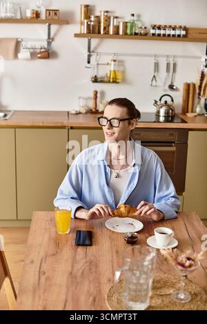 A young man with feminine features smiles while having breakfast at a cozy kitchen table. Stock Photo
