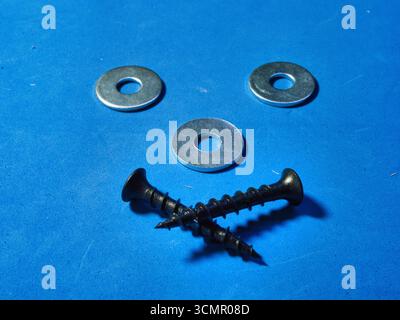 Funny face made with screws and washers on blue background - A creative and playful composition forming a smiling face with industrial hardware on a v Stock Photo