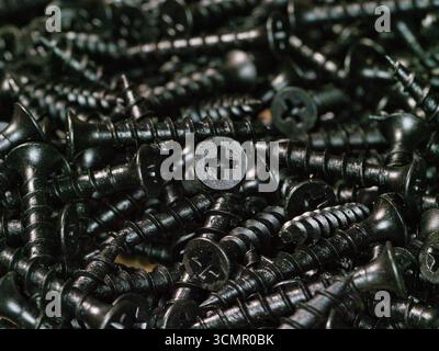 Macro view of black drywall screws background - A detailed, close-up view of a pile of black drywall screws, creating a textured and industrial backgr Stock Photo