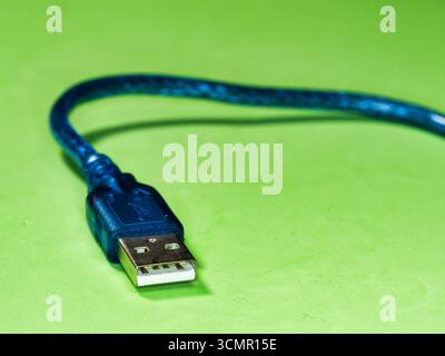 Blue USB cable on a vibrant green background - A single, blue USB Type-A cable with a gold-colored tip rests on a bright green surface, creating a bol Stock Photo