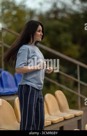 brunette girl stands alone in an empty stadium dressed in a blue t shirt. With her hair flowing she shows excitement and joy celebrating a hard earned victory in the fresh air. Stock Photo