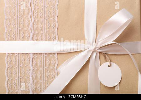Gift box wrapped in kraft paper with blank tag as background, closeup Stock Photo