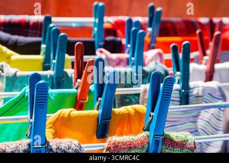 Multi-colored clothes hang attached to clothespins and dry after washing, close-up. Stock Photo