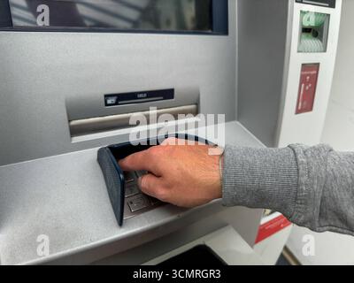 Bavaria, Germany - September 17, 2025: A man withdraws cash from an ATM with his debit card. He covertly enters the PIN or secret code *** Ein Mann hebt mit seiner EC-Karte Bargeld an einem Geldautomaten ab. Er gibt verdeckt die PIN bzw. Geheimzahl ein Stock Photo