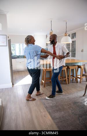Senior African American couple holding hands and dancing in home kitchen at wooden island Stock Photo
